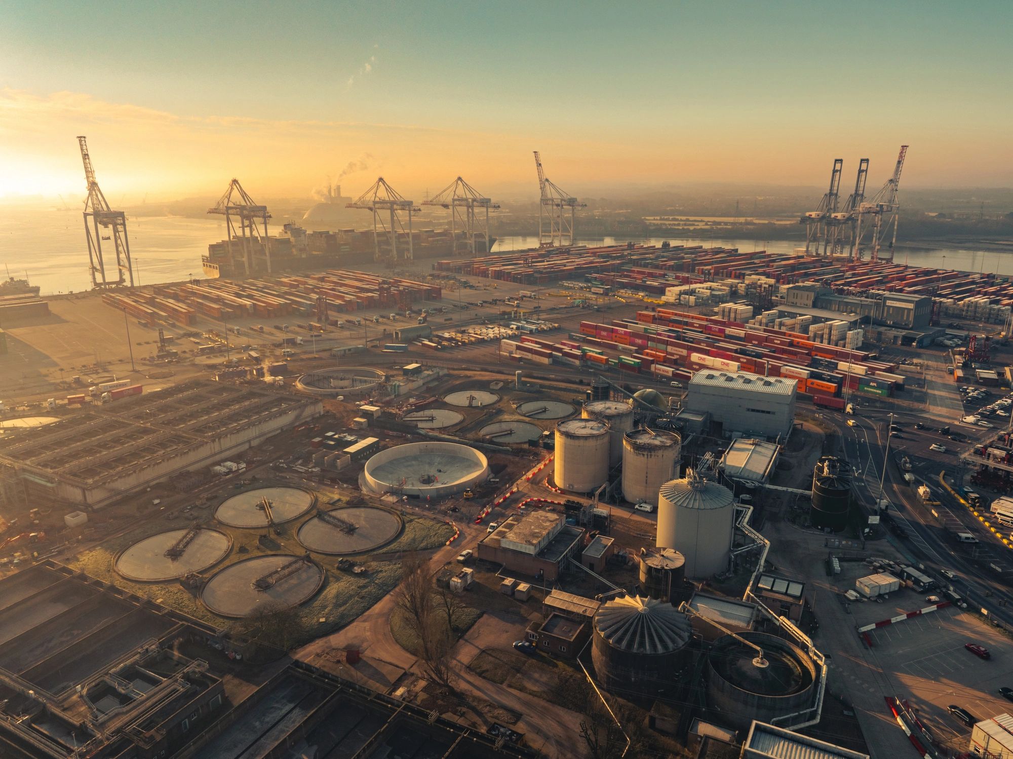 Commercial port terminal with containers, cranes, and industrial infrastructure at sunset